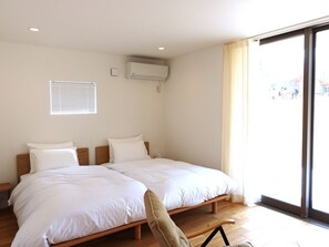 Una cama doble con ropa de cama blanca, una mesita de noche pequeña y una ventana con persianas.