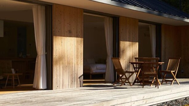 Una casa moderna con terraza de madera, ventanas amplias y comedor con sillas.