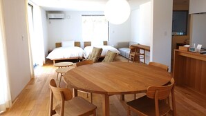 Amplia habitación con una gran mesa de comedor de madera rodeada de sillas, un conjunto de sofás y una cama.