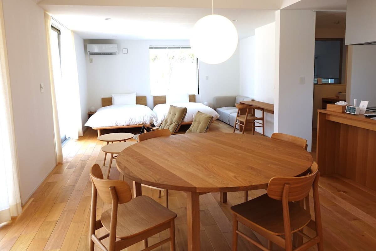 Amplia habitación con una gran mesa de comedor de madera rodeada de sillas, un conjunto de sofás y una cama.