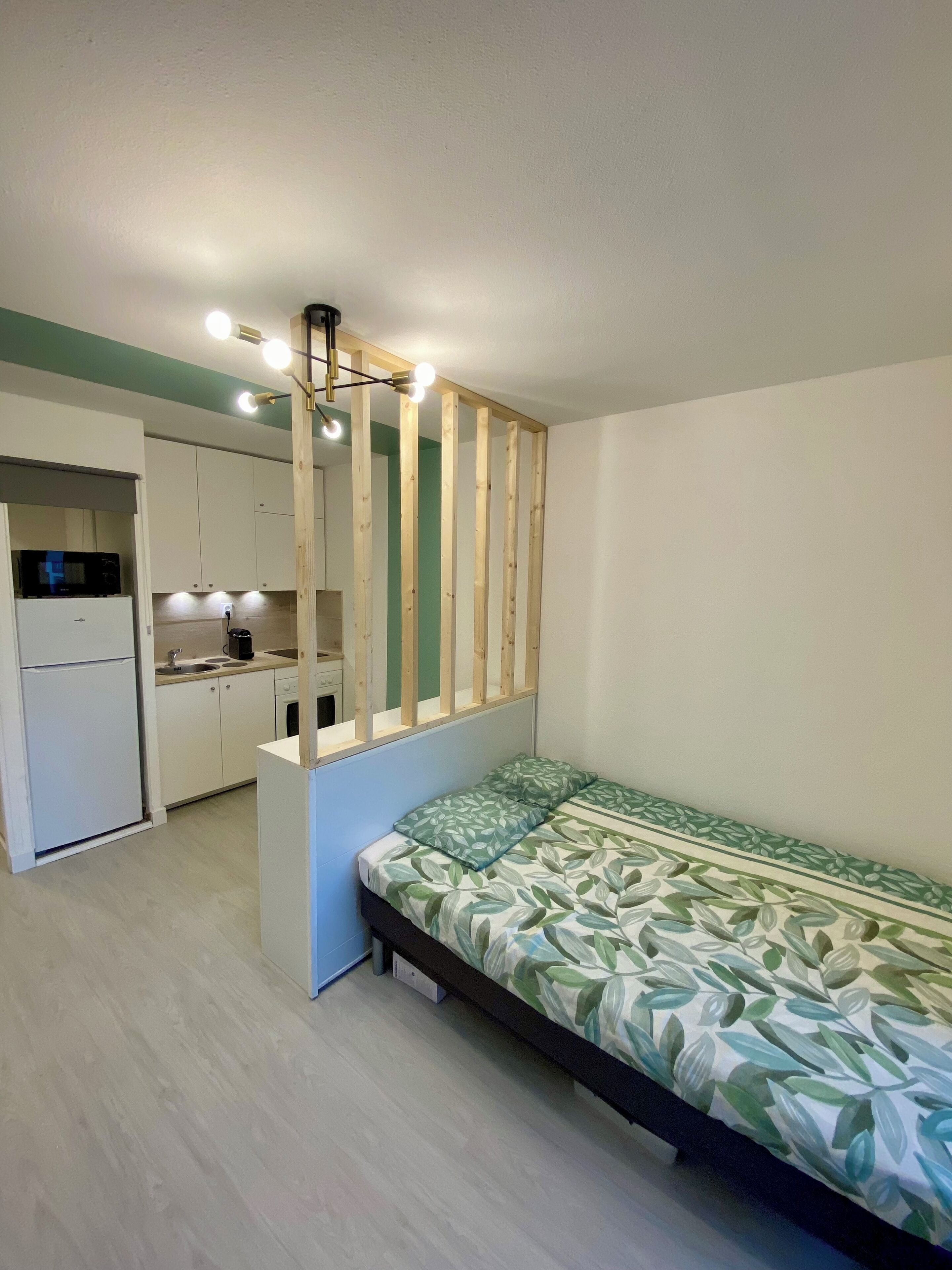 A compact room with a bed, kitchenette, and a wooden partition.
