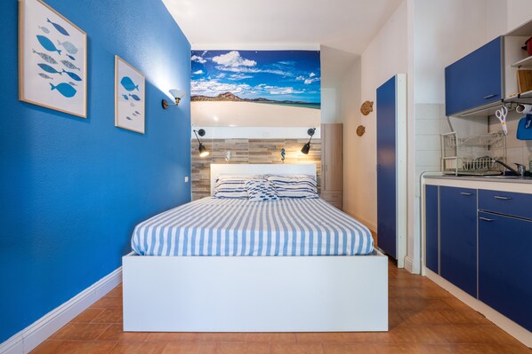 A bedroom with a bed, a wall mural, a kitchen area, and a bathroom.