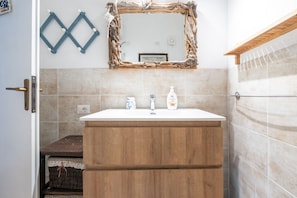 Un bagno con un mobile bagno in legno, uno specchio con cornice naturale e un portasciugamani.