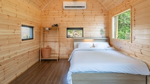 Een houten kamer met een bed, een plankje met een mand, en een raam.