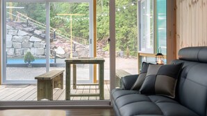 Een modern interieur met een houten bank, een zwarte bank en grote ramen met uitzicht op een stenen trap en groen buiten.
