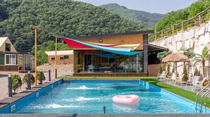 Un espace piscine moderne offrant une vue dégagée sur la piscine, des chaises longues et un bâtiment en bois doté de grandes fenêtres.