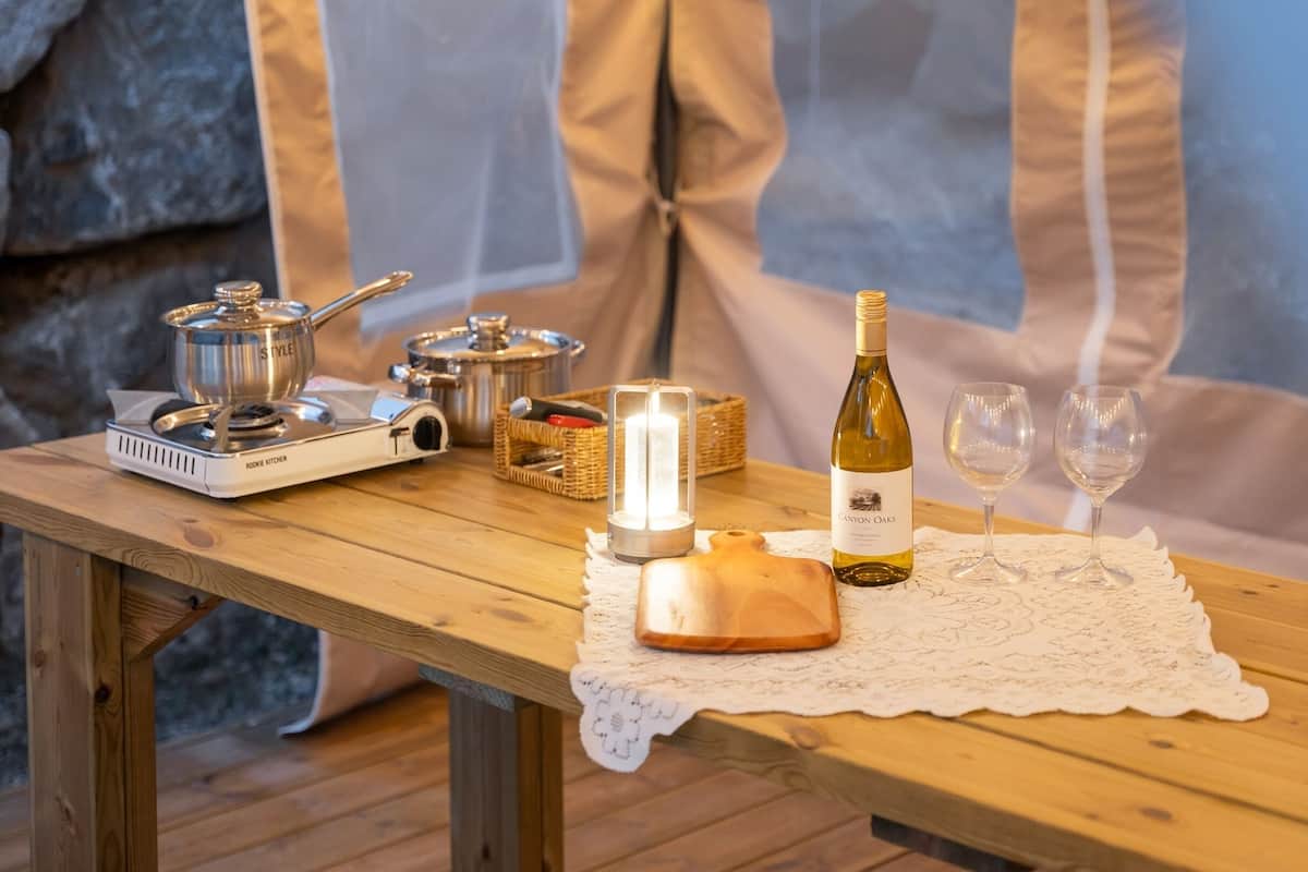 Ein Holztisch mit einem tragbaren Kocher, einer Weinflasche, zwei Gläsern und einer Kerze.