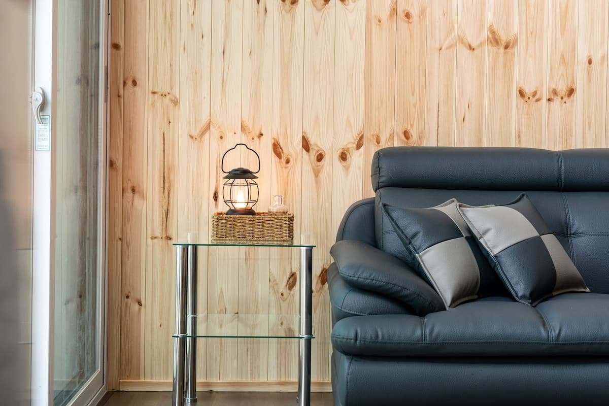 Ein modernes Wohnzimmer mit einem dunkelbraunen Ledersofa, einem Glastisch und einer Holzwand.