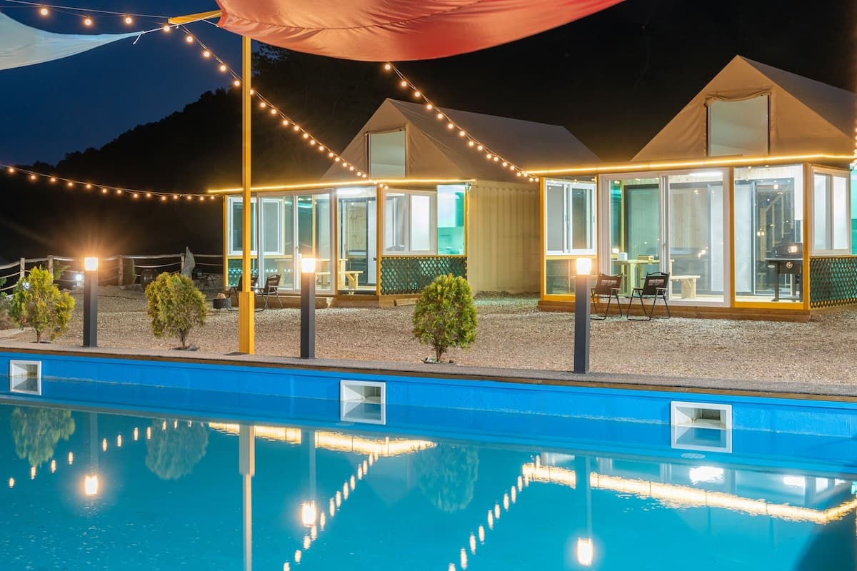 Blick auf einen Poolbereich eines Hotels mit mehreren Zimmern unter Glasdächern, Lichterketten und einer Zelthalle.