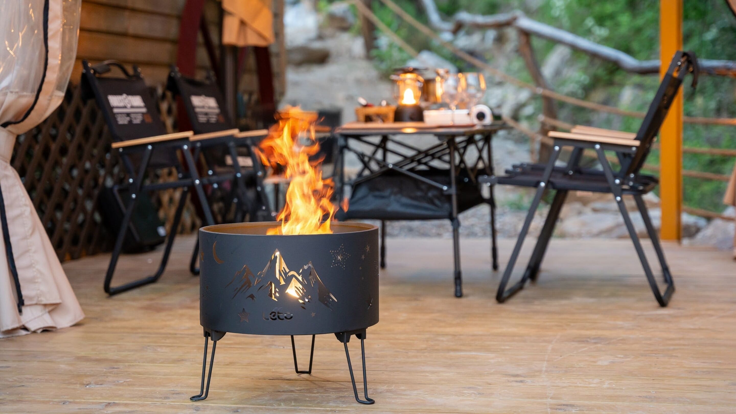 A campfire in a metal container with a star design, surrounded by outdoor furniture and a wooden deck.