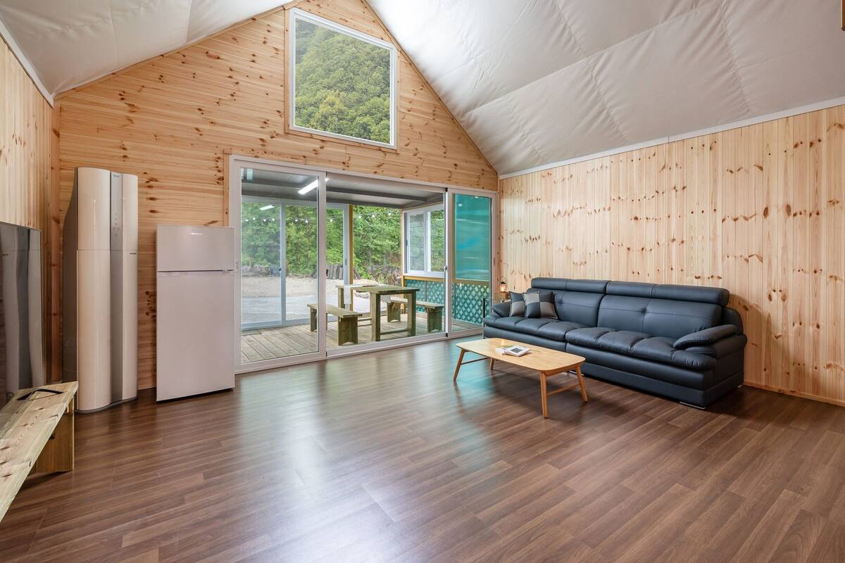 Ein gemütliches Blockhaus mit Holzvertäfelung, einer schwarzen Couch, einem Holztisch und einer Glastür zum Außenbereich.