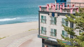A 7-Eleven store adjacent to a beach with a building featuring balconies and a view of the ocean. - Samcheok Kong & Bee Ocean View Spa Pensi (Samcheok)