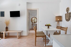Un espace repas moderne avec une table blanche, deux chaises en bois, un banc, un téléviseur et un miroir fixé au mur.