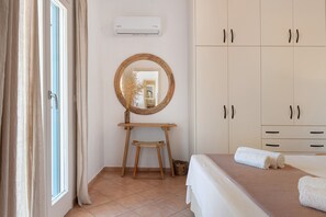 Une chambre à coucher avec un lit, un tabouret en bois, un miroir rond et une armoire.