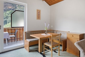 Una habitación con una mesa de madera, asientos tipo banco, un mueble pequeño y una ventana con vistas a vegetación.