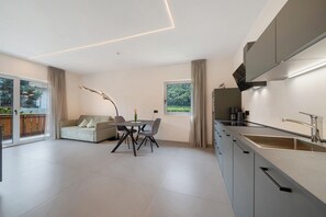Une cuisine moderne dotée d’un four encastré, un coin repas avec une table et des chaises, et une grande fenêtre offrant une vue sur la verdure.