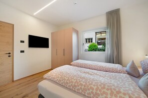 A bedroom with two beds, a TV, a wardrobe, and a window with a view of greenery. - Apartment 'Rosalie  5' with Mountain View, Shared Pool and Wi-Fi (Lana)