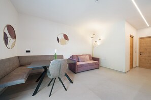A modern living room with a sofa, a dining table, and a chair. There are two wall-mounted mirrors and a floor lamp. - Apartment 'Rosalie  5' with Mountain View, Shared Pool and Wi-Fi (Lana)