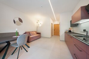 A modern kitchen with a built-in oven, a dining area with a table and chairs, and a living area with a sofa and a wall-mounted light fixture. - Apartment 'Rosalie  5' with Mountain View, Shared Pool and Wi-Fi (Lana)