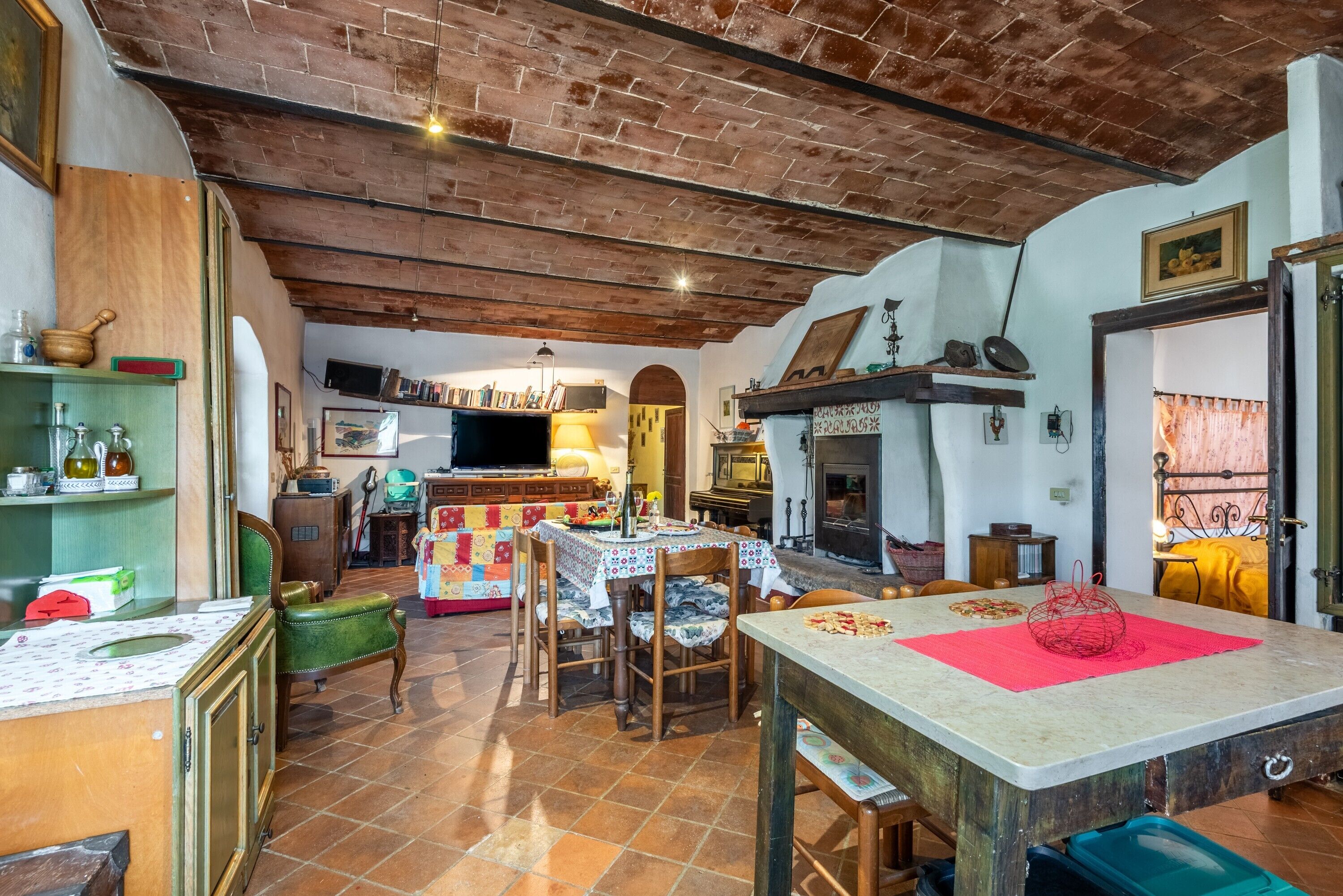 A rustic interior with exposed brick ceilings, a dining area with a table and chairs, a fireplace, and a kitchen area with a stove.