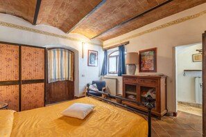Un dormitorio con cama, armario de madera, una silla, un mueble y una ventana con cortinas.