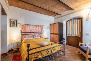 Un dormitorio con cama, armario de madera, una mesita de noche con lámpara y una puerta con cortina a rayas.
