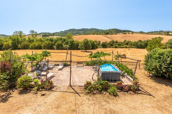 Un patio trasero con piscina, mobiliario exterior y una pérgola.