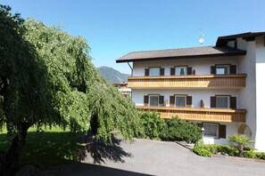 A multi-story building with balconies, a driveway, and a tree in the foreground. - Apartment 'Rosalie  3' with Mountain View, Shared Pool and Wi-Fi (Lana)