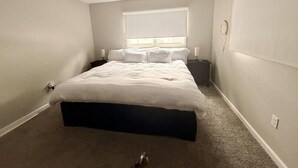 Un dormitorio con cama, ventilador de techo, ventana y mesita de noche.
