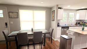 Una cocina moderna con armarios blancos, una mesa de comedor con cuatro sillas y una pequeña isla con un fregadero.