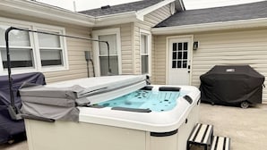 Un jacuzzi con tapa, escalones y una parrilla frente a una casa.