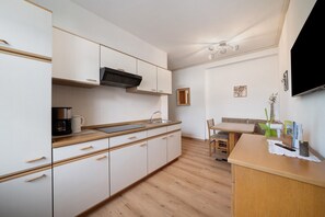 A modern kitchen with white cabinets, a wooden countertop, a built-in microwave, and a dining area with a table and chairs.