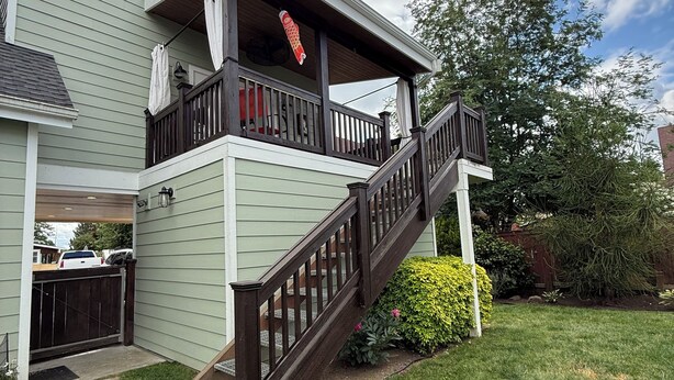 Une maison à deux étages avec un escalier en bois menant à un balcon, une cour arrière clôturée et une pelouse bien entretenue.