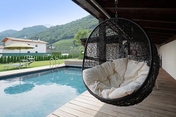 Una silla colgante junto a una piscina, con vista a una casa y montañas.