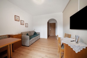 Una sala de estar con un sofá, una mesa de madera y un televisor montado en la pared.