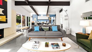 A modern living room with a grey sofa, a coffee table with magazines, and a green armchair. - The Butterfly Alexander  – Stylish Mid-Century Home with Pool, Spa, Views & Fire Pit (Palm Springs)