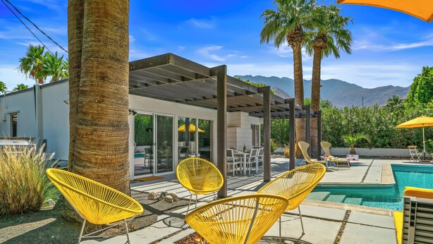 A poolside area with yellow chairs, a pergola, and a view of mountains. - The Butterfly Alexander  – Stylish Mid-Century Home with Pool, Spa, Views & Fire Pit (Palm Springs)