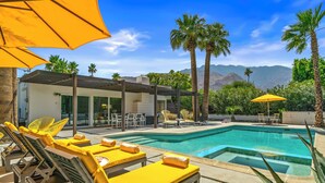 A pool area with sun loungers and umbrellas, surrounded by palm trees and mountains in the background. - The Butterfly Alexander  – Stylish Mid-Century Home with Pool, Spa, Views & Fire Pit (Palm Springs)