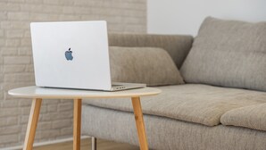 Um laptop sobre uma pequena mesa redonda, em frente a um sofá.