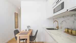 Cozinha compacta com bancada de mármore, pia e pequena área de refeições com mesa e cadeiras.