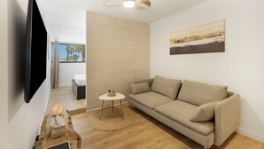 Uma sala de estar moderna com televisão de tela plana, sofá bege, mesa de centro redonda e piso de madeira.