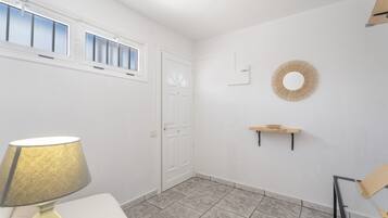 Een kamer met een witte deur, een raam met jaloezieën, een lamp, een wandplank en een ronde decoratie aan de muur.