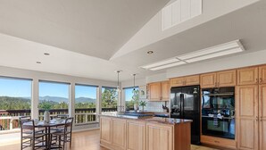 A modern kitchen with large windows, a dining area, and a view of the mountains. - Downtown Close Lake View with Tesla Charging (Coeur D Alene)