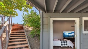 A small, single-room cabin with a wooden staircase leading to a door. Inside, there's a bed with a checkered blanket and a television on a stand. - Downtown Close Lake View with Tesla Charging (Coeur D Alene)
