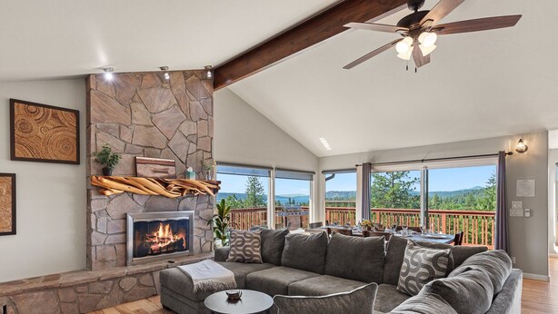 A spacious living room with a stone fireplace, a ceiling fan, and a view of the outdoors. - Downtown Close Lake View with Tesla Charging (Coeur D Alene)