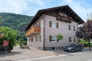 Ein mehrstöckiges Gebäude mit Balkonen, ein Auto davor und eine Bergkulisse im Hintergrund.