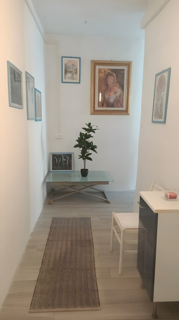 A hallway with a bench, a potted plant, a rug, and framed pictures on the walls.