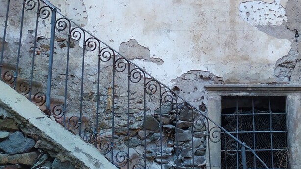A building with two windows, a stone staircase, and a metal railing.