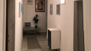 A hallway with a desk, a potted plant, framed pictures on the walls, and a white cabinet.
