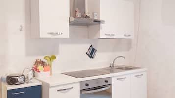 Een koelkast, een oven, een kookplaat, kookgerei, borden en bestek